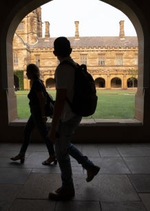 Image of shadowed university students walking through open corridor alongside university quadrangle