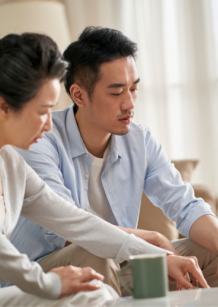 A man and his mother seated on the couch looking over papers on the coffee table