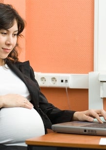 Pregnant lady sitting in front of her laptop with hand over her baby bump