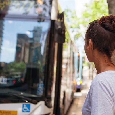 A young woman waits for a bus on a city street.