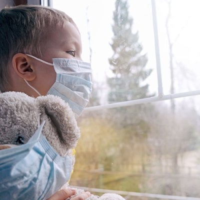 Sad child in quarantine with mask and masked teddy bear