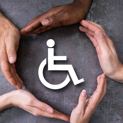 A group of hands, all with different coloured skin tones, create a circle around a sign for disability.