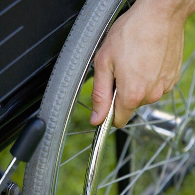 A close-up view of one wheel of wheelchair. A person is holding the wheel. 