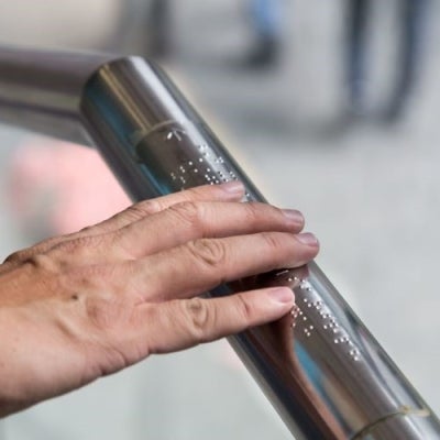 Image of a hand reading braille on a railing 