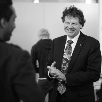 Black and white image of Simon speaking with others. He is wearing a suit