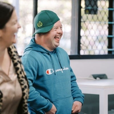 Two people side on smiling and laughing. The man is wearing a Woolworths hat. 