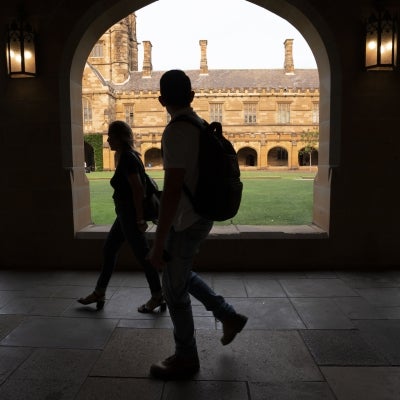 Image of shadowed university students walking through open corridor alongside university quadrangle