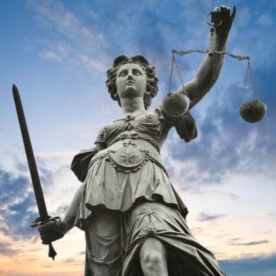 Outdoor metal statue of Justice with sky in background.
