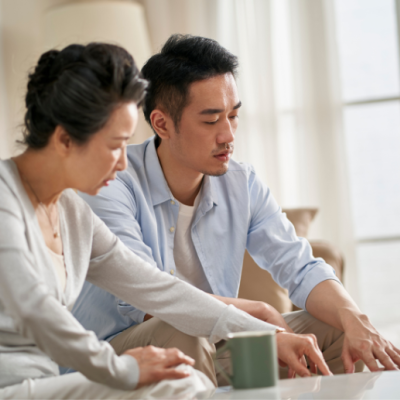 A man and his mother seated on the couch looking over papers on the coffee table