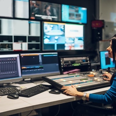 Middle aged woman in blue shirt sitting at a desk using equipment in control room on a TV station