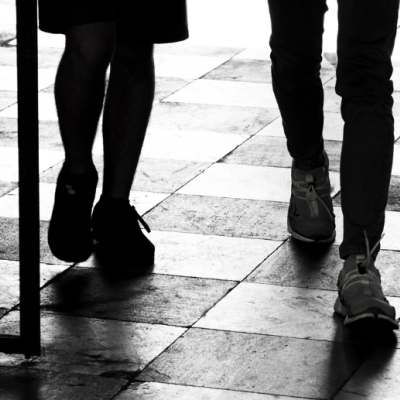 Black and white image showing the legs of a schoolboy and girl as they walk on chequered tiles.