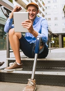 A person with a prosthetic limb sits smiling as they look at their eTablet